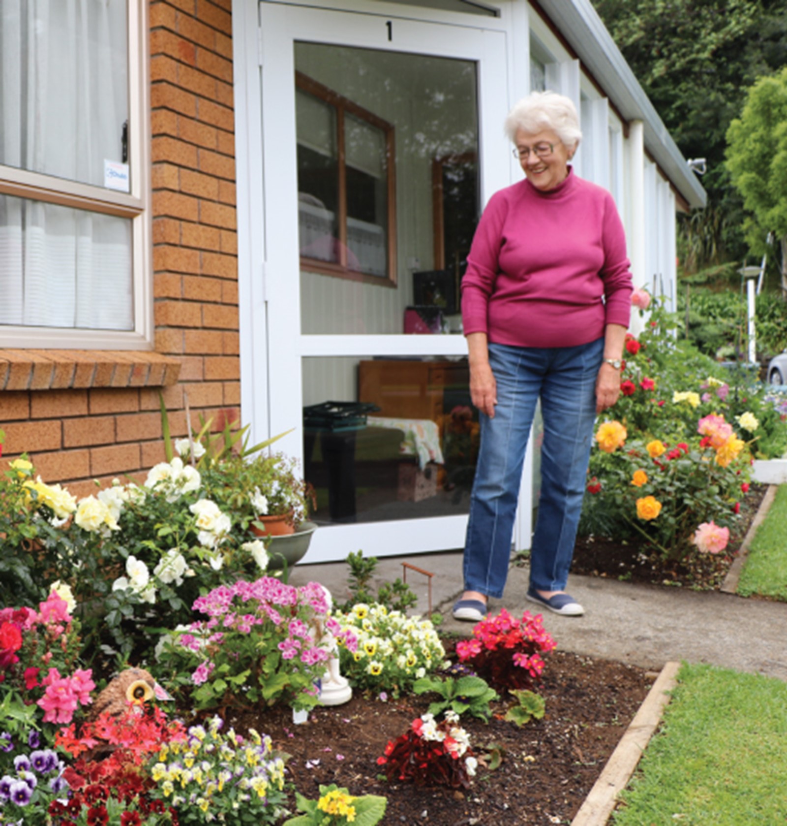Elderly woman outside of her Council flat with flower garden